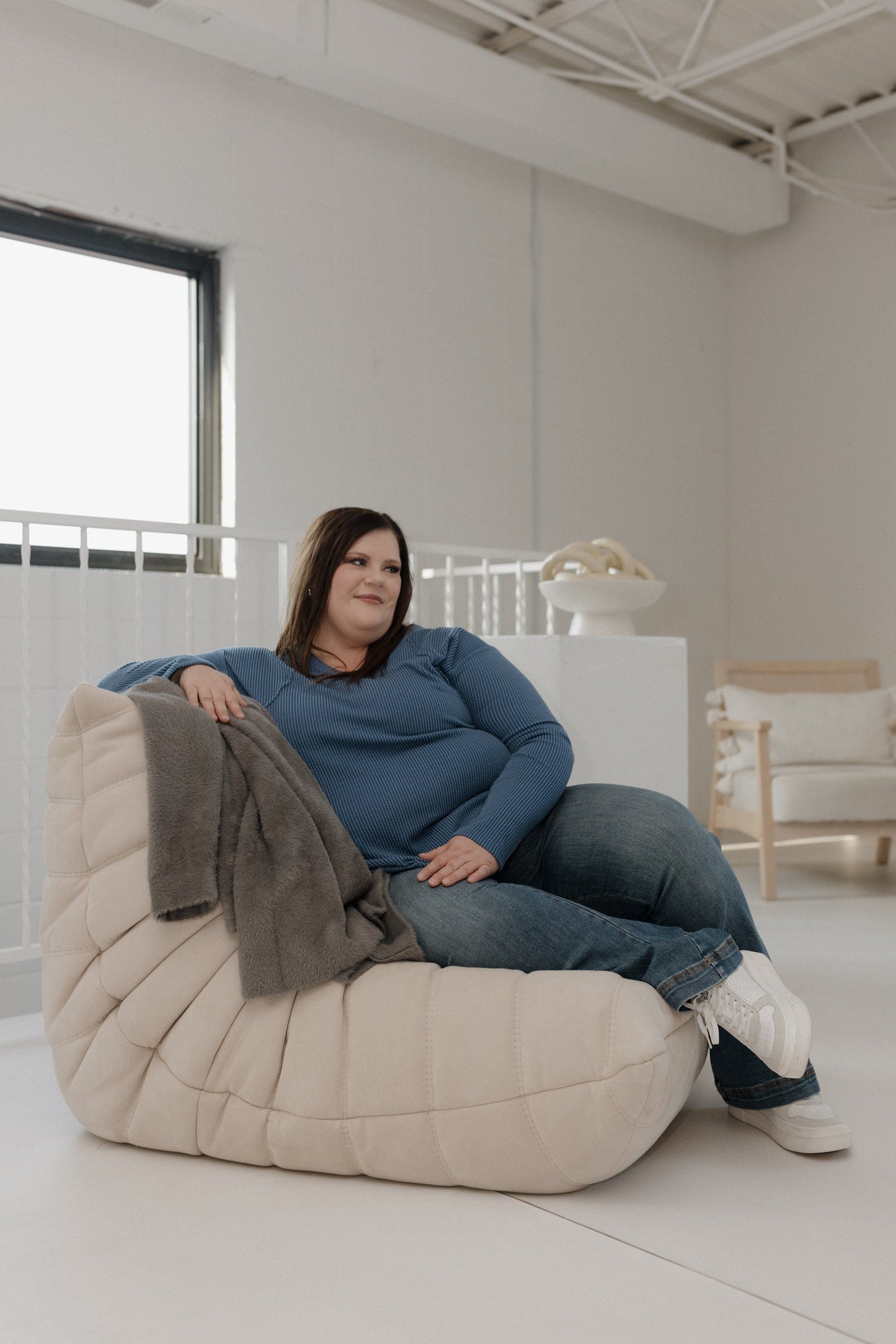 Woman sitting on a bean bag chair in a modern, minimalistic room.