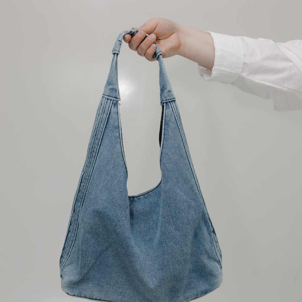 Blue denim bag held by a hand against a plain background