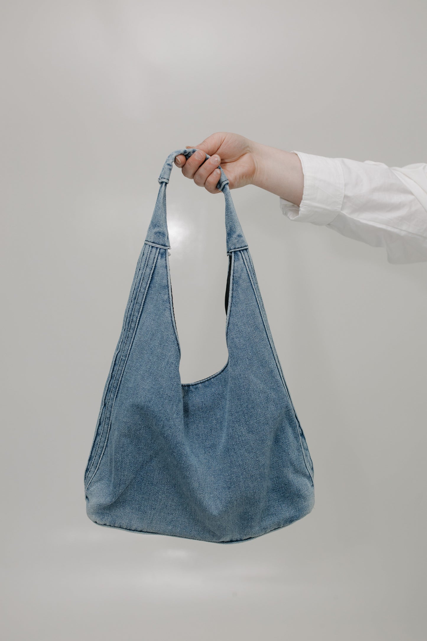 Blue denim bag held by a hand against a plain background