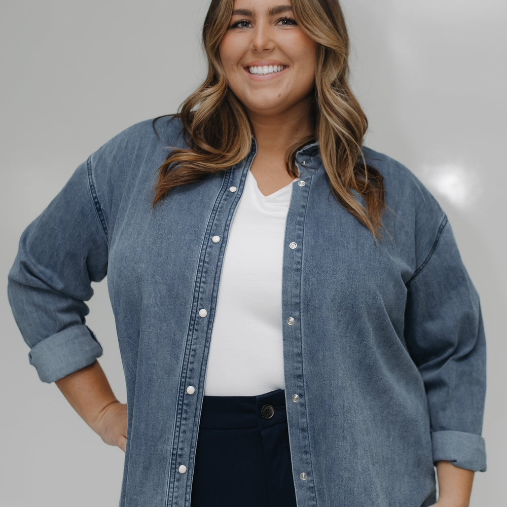 Woman wearing a denim jacket over a white shirt with a neutral background