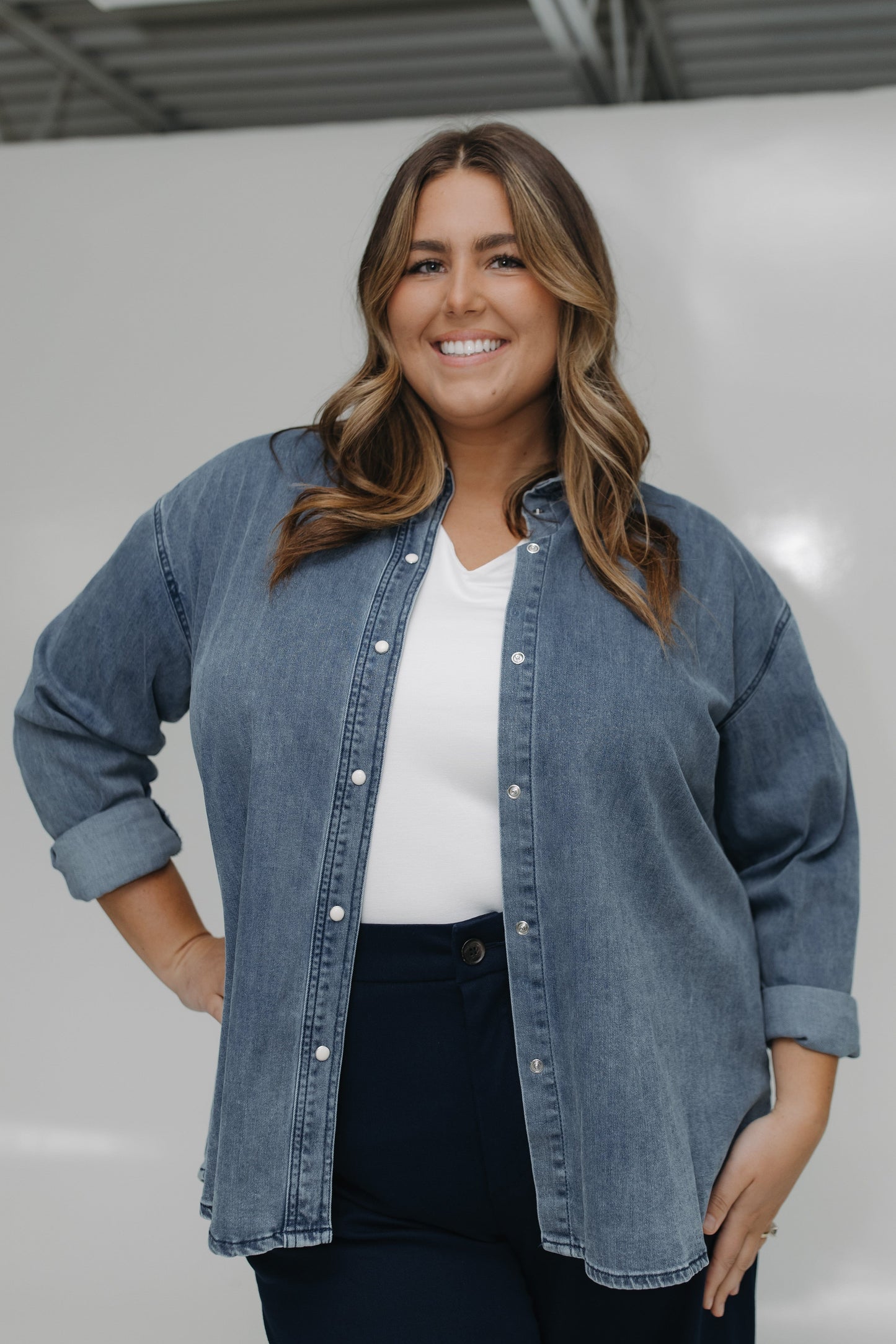 Woman wearing a denim jacket over a white shirt with a neutral background