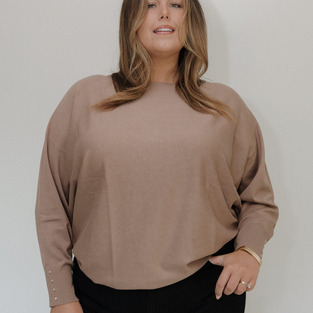 Woman wearing a beige sweater and black pants against a white background
