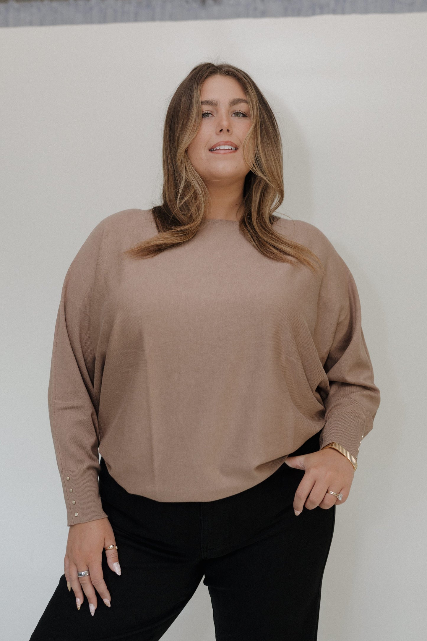 Woman wearing a beige sweater and black pants against a white background