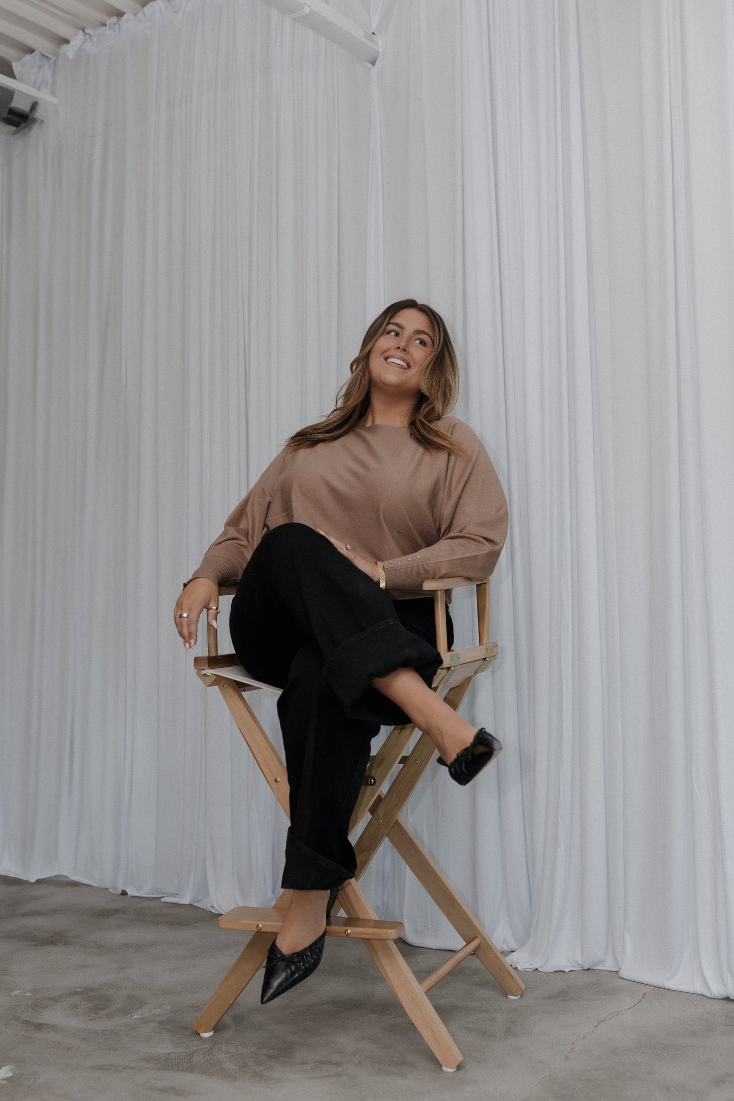 Woman sitting on a director's chair against a white curtain backdrop