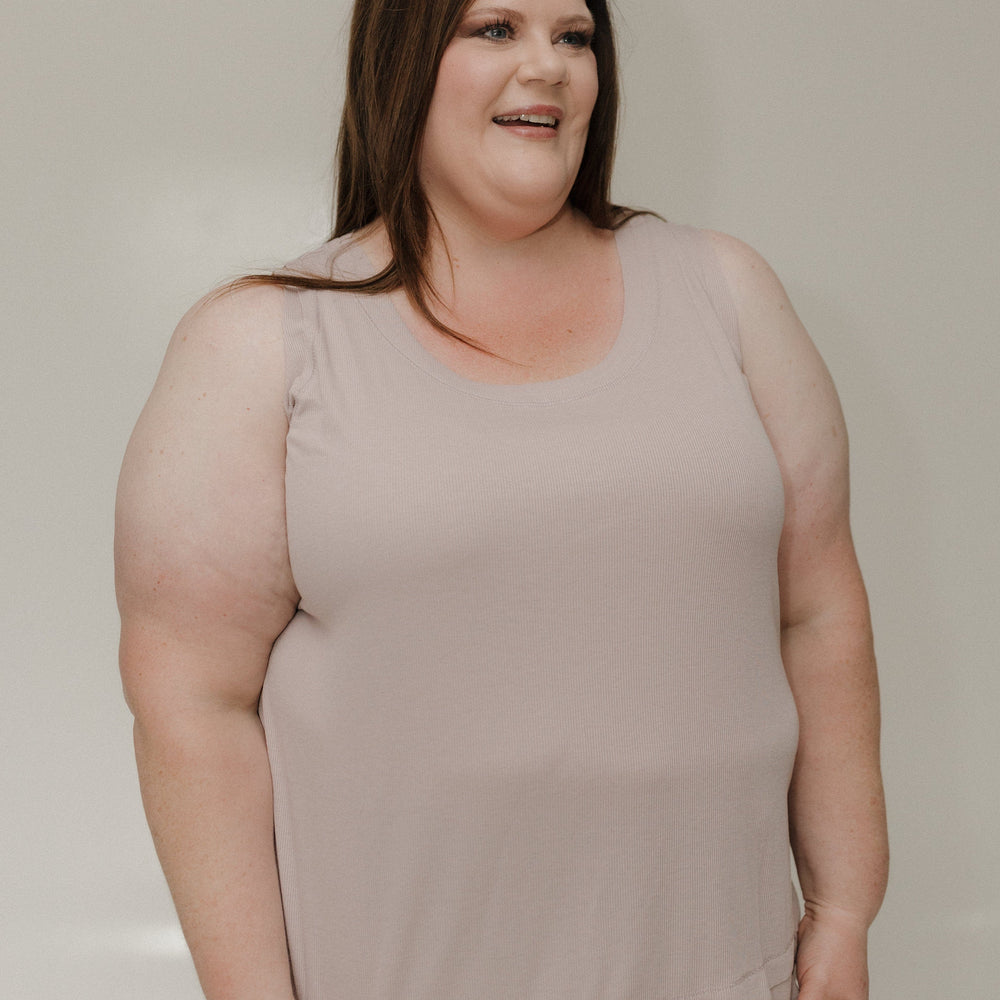 Woman wearing a beige sleeveless top against a plain background