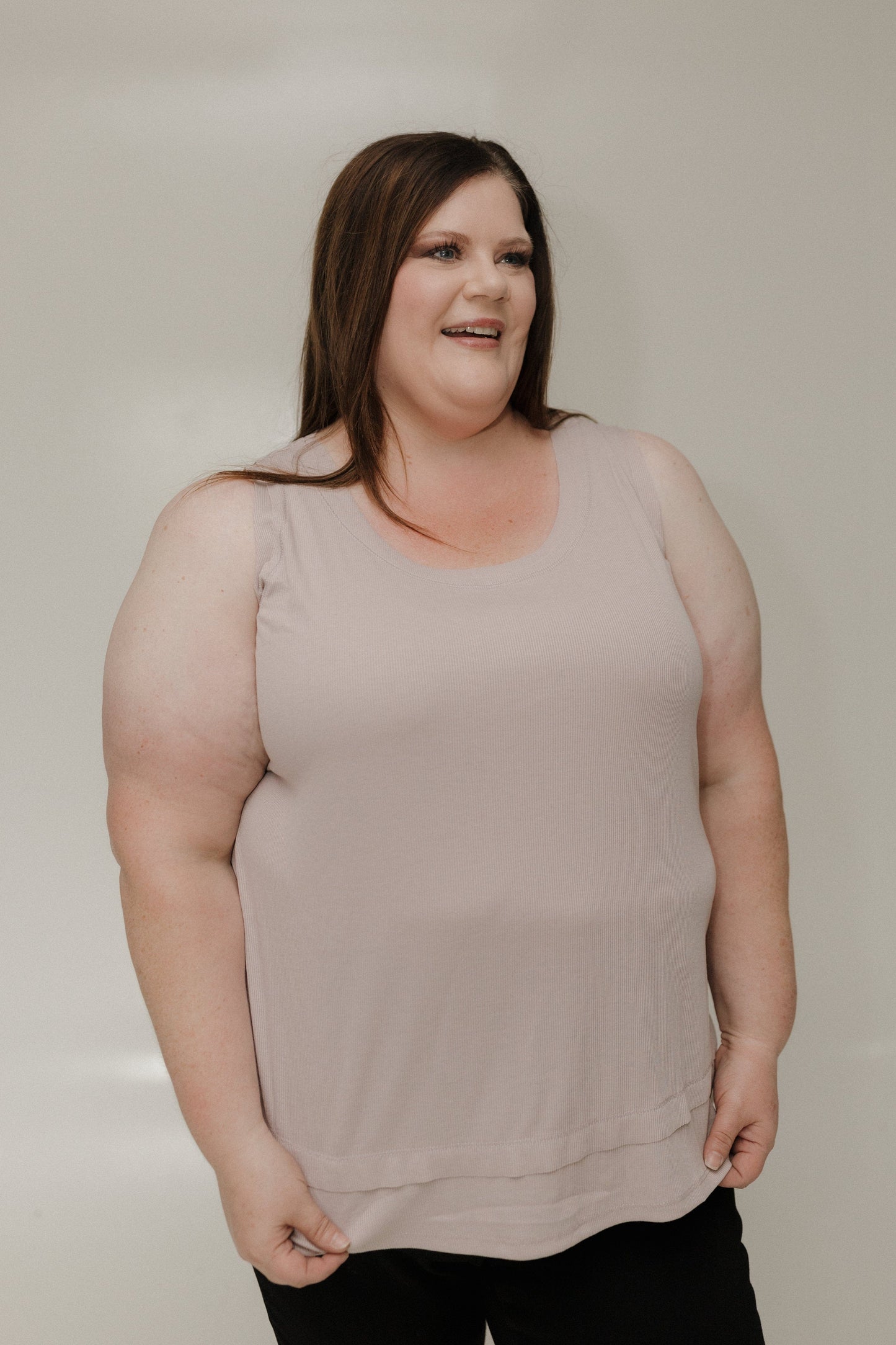 Woman wearing a beige sleeveless top against a plain background