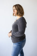 A person wearing a dark gray DOUBLE PEEK-A-BOO 3/4 SLEEVE TEE from Love Marlow, featuring criss-cross cutout details on the back, stands facing away from the camera.