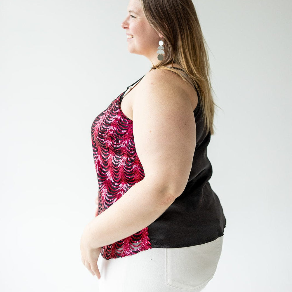 A person with long hair, wearing a sleeveless red and black top featuring adjustable straps and white pants, stands in profile against a plain white background.