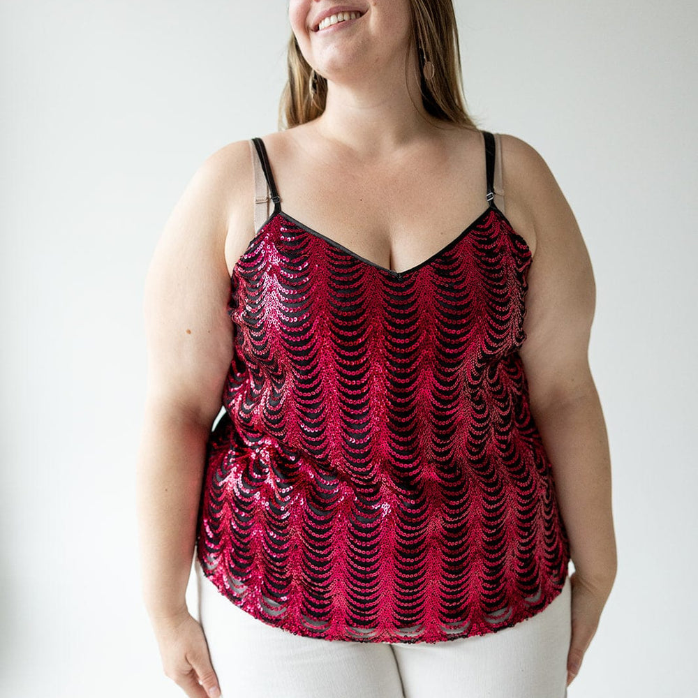 A woman in a hot pink, double V-neck sequin cami with adjustable straps and white pants smiles against a plain background.