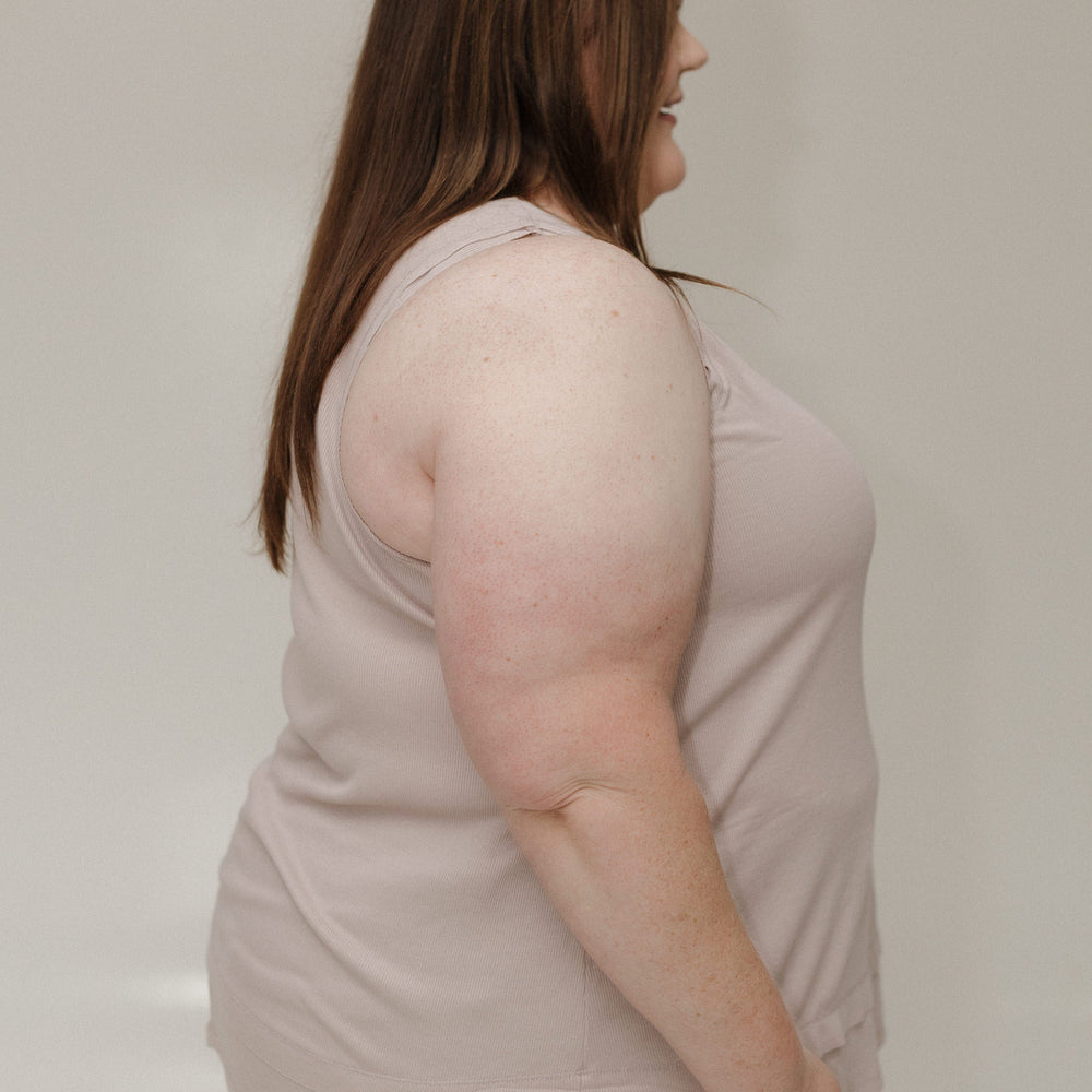 Woman wearing a light pink sleeveless top against a plain background