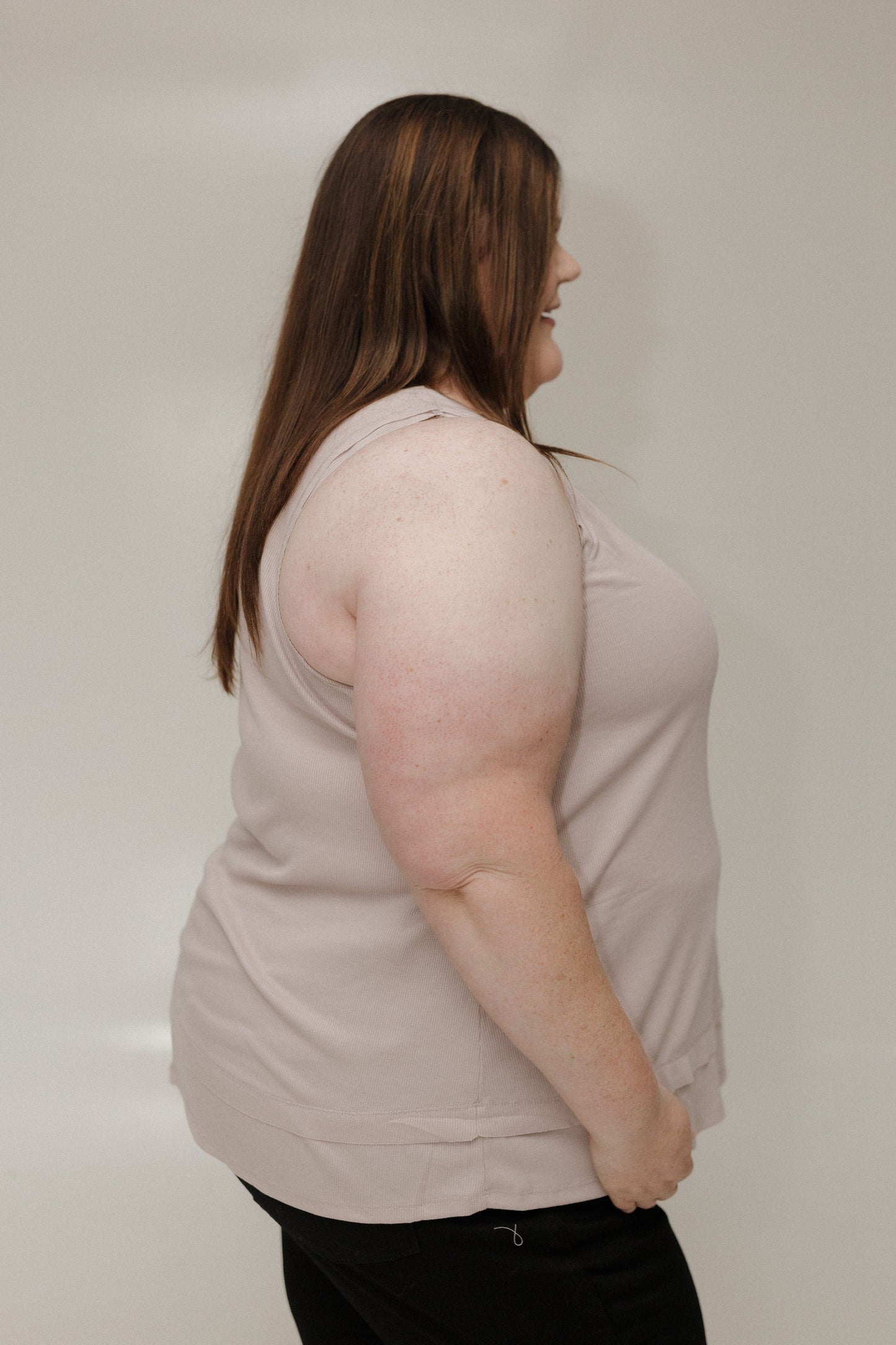 Woman wearing a light pink sleeveless top against a plain background