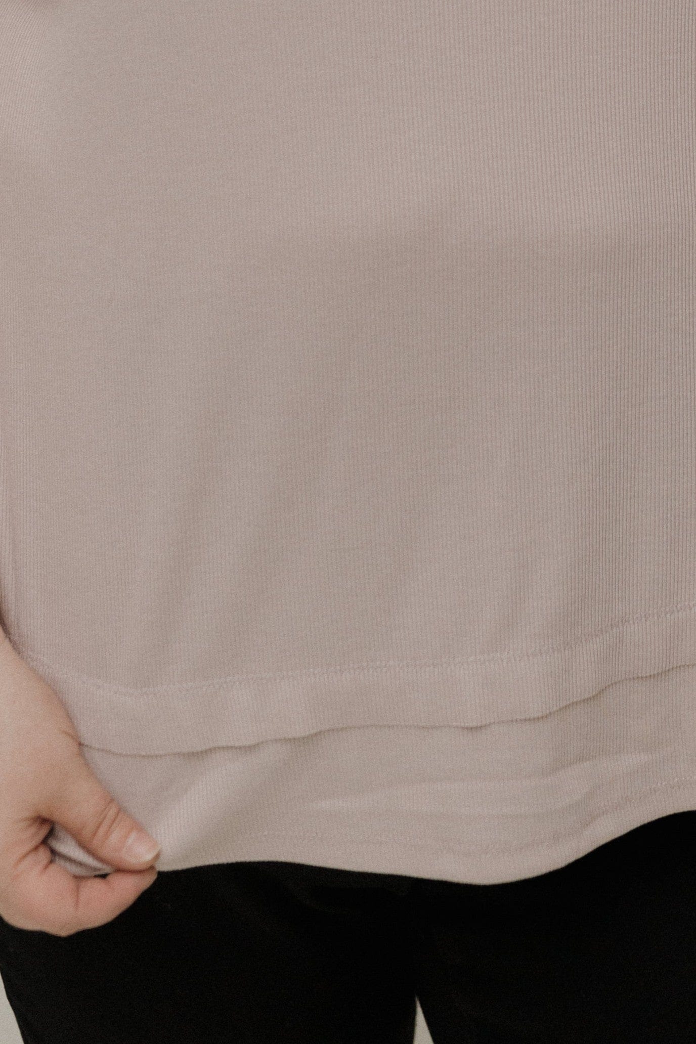 Close-up of a beige shirt with a hand adjusting it, on a plain background
