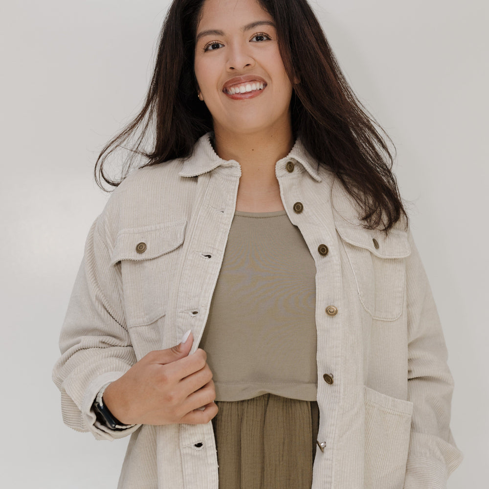 Woman wearing a beige jacket and green dress against a white background