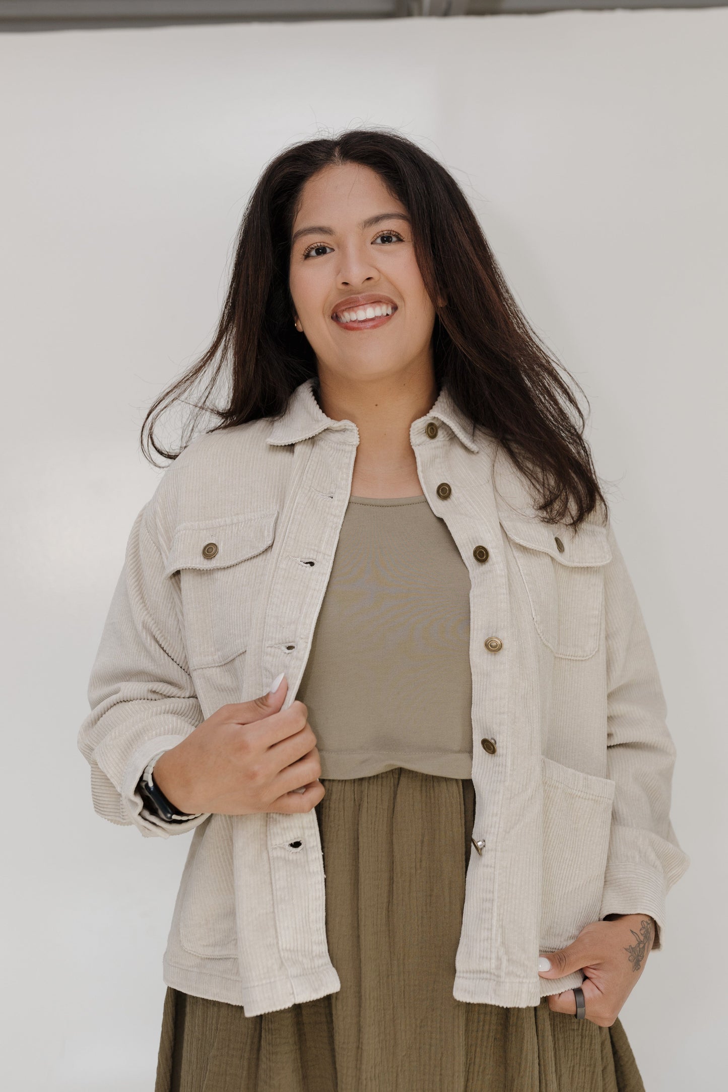 Woman wearing a beige jacket and green dress against a white background