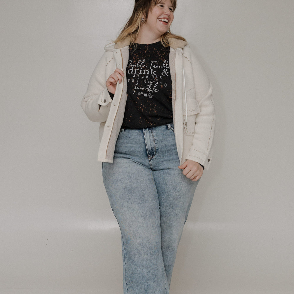 "DOUBLE TROUBLE DRINK AND STUMBLE CLINK THE GLASS TRY NOT TO STUMBLE" GRAPHIC TEE Woman wearing a black long-sleeve shirt with text and light blue jeans on a plain background at Love Marlow