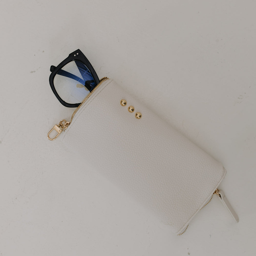 White pouch with gold zipper and black glasses on a white background