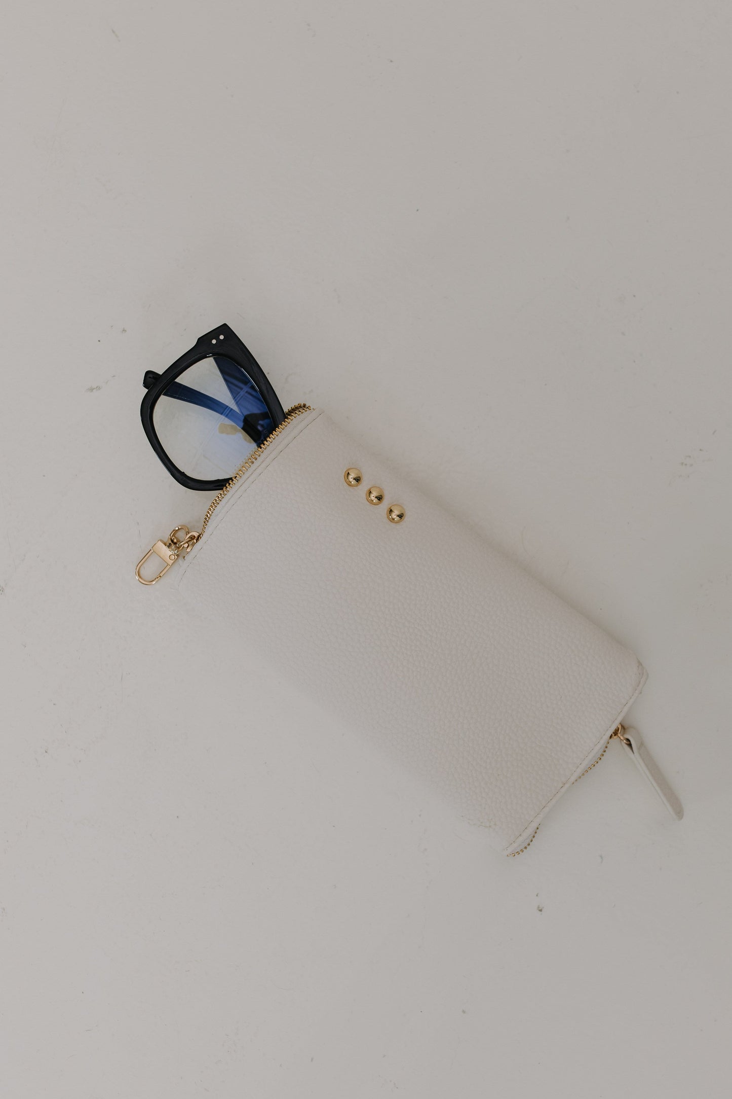 White pouch with gold zipper and black glasses on a white background