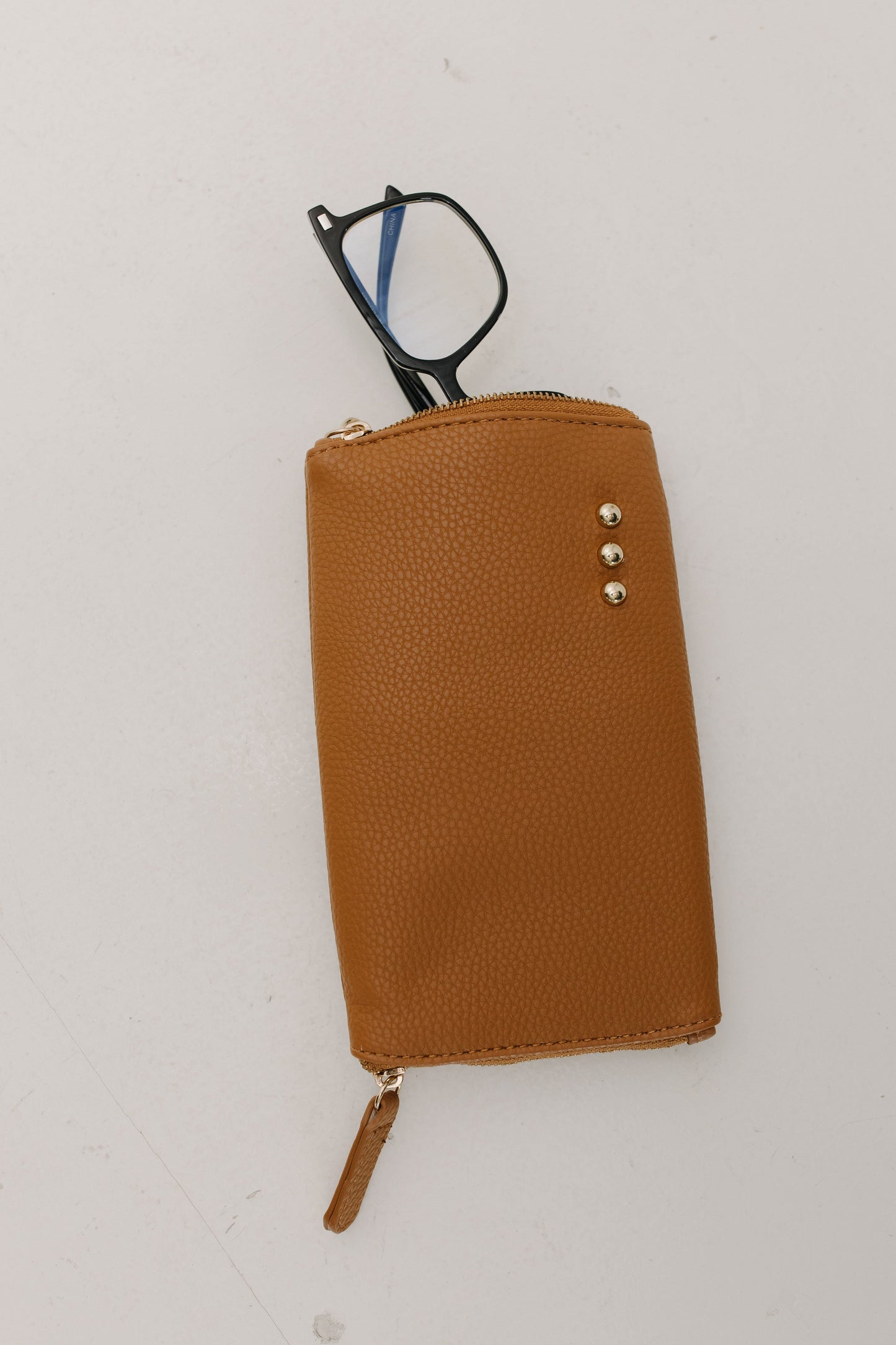 Brown leather case with a zipper containing eyeglasses on a white background