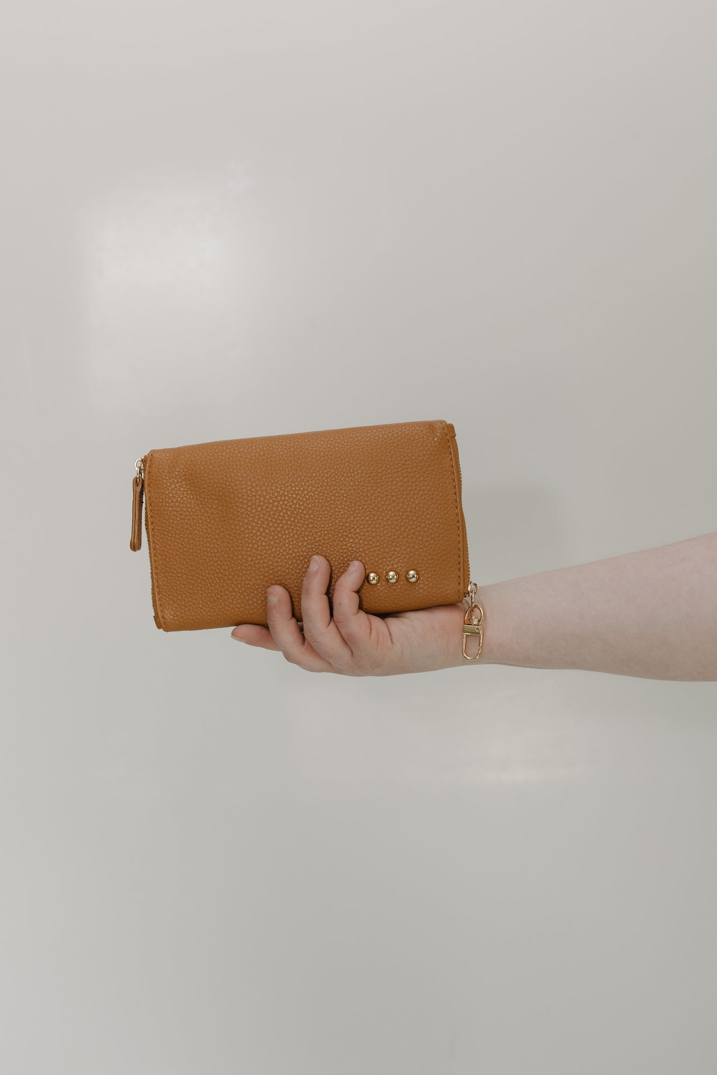 Brown clutch held by a hand against a plain background