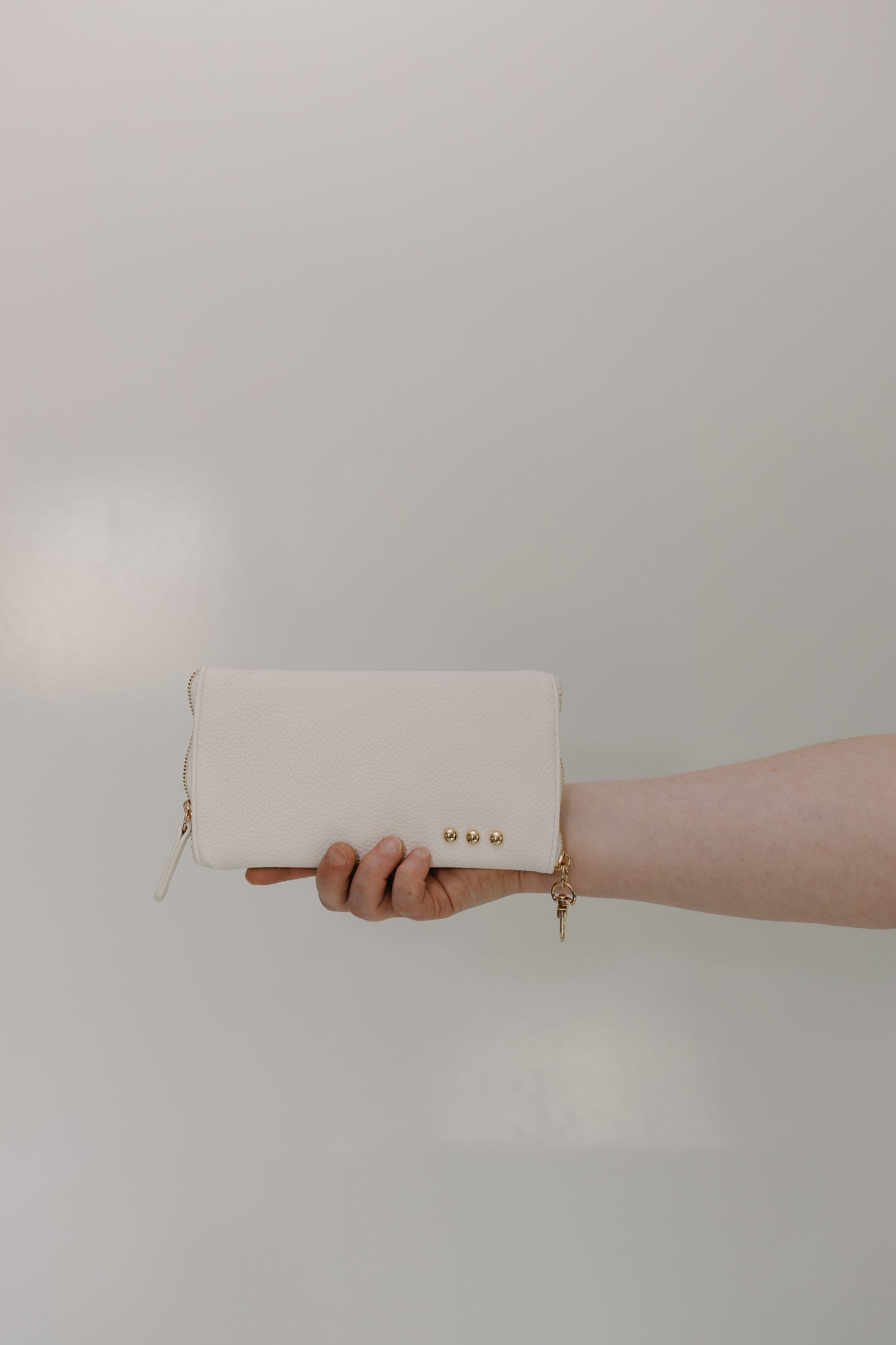 White clutch held by a hand against a plain background