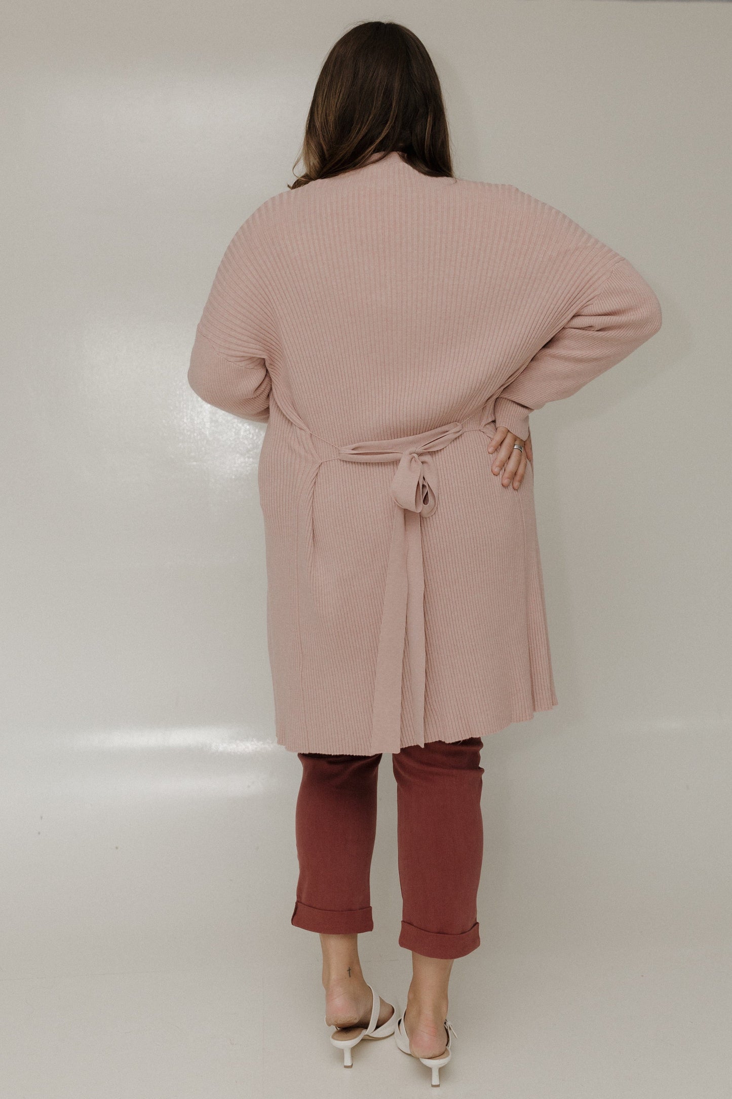 Person wearing a pink coat and brown pants against a white background