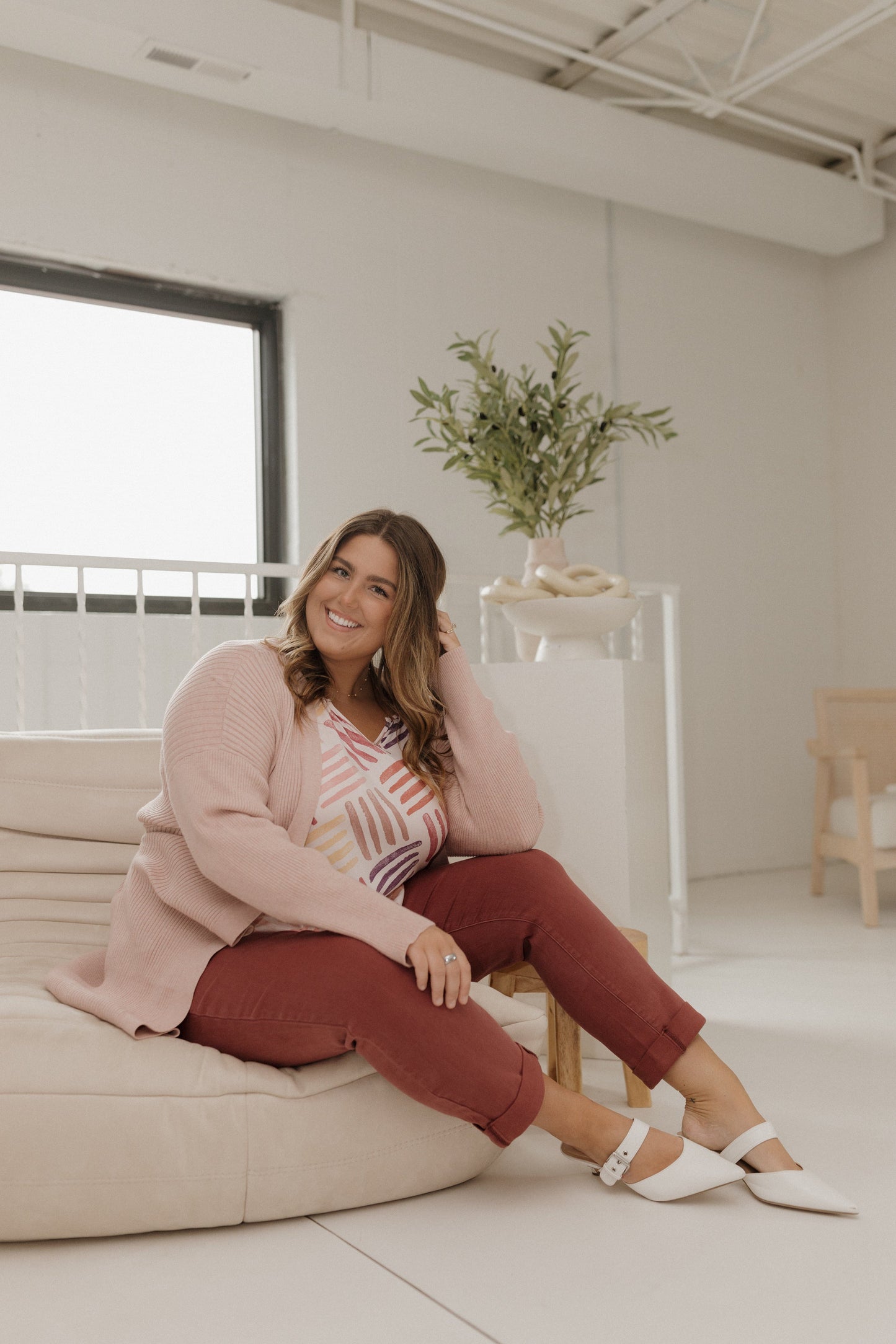 Woman sitting on a couch in a bright, minimalistic room with a plant in the background.