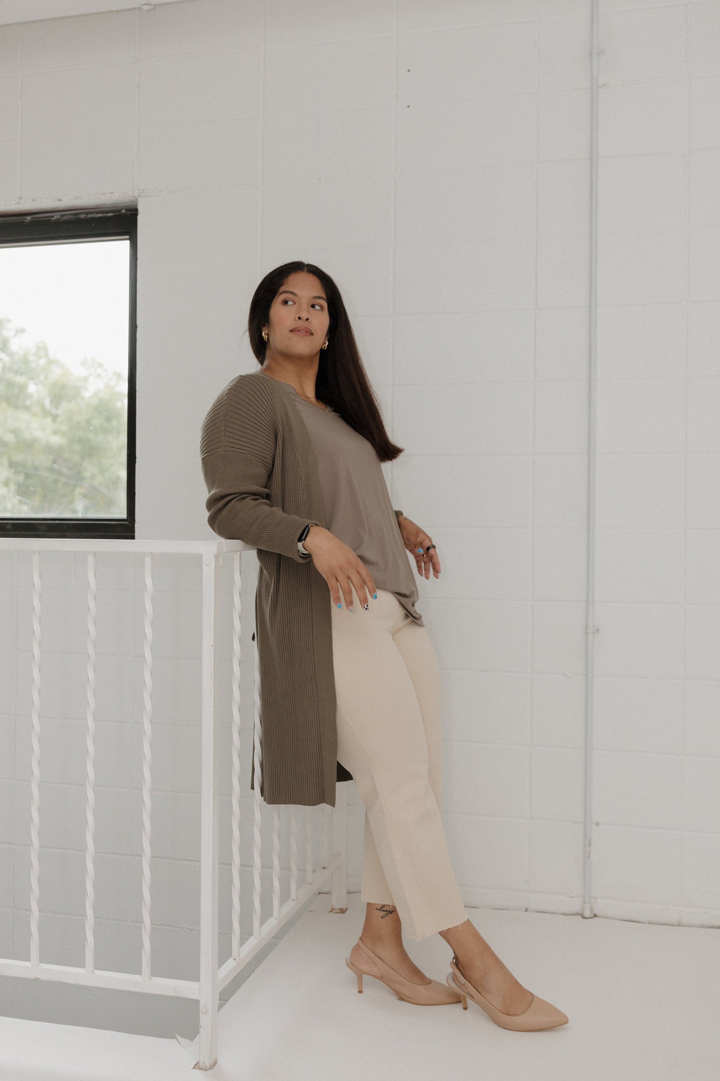 Woman standing in a minimalistic room with white walls and a window.