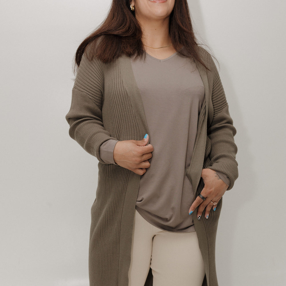Woman wearing a long olive green cardigan over a beige top and pants on a white background
