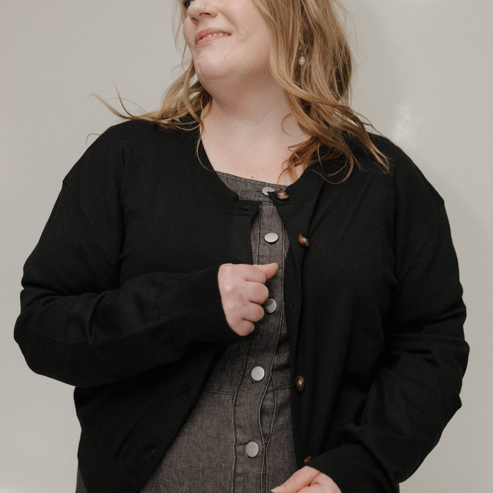 Woman wearing a black cardigan over a gray dress against a plain background