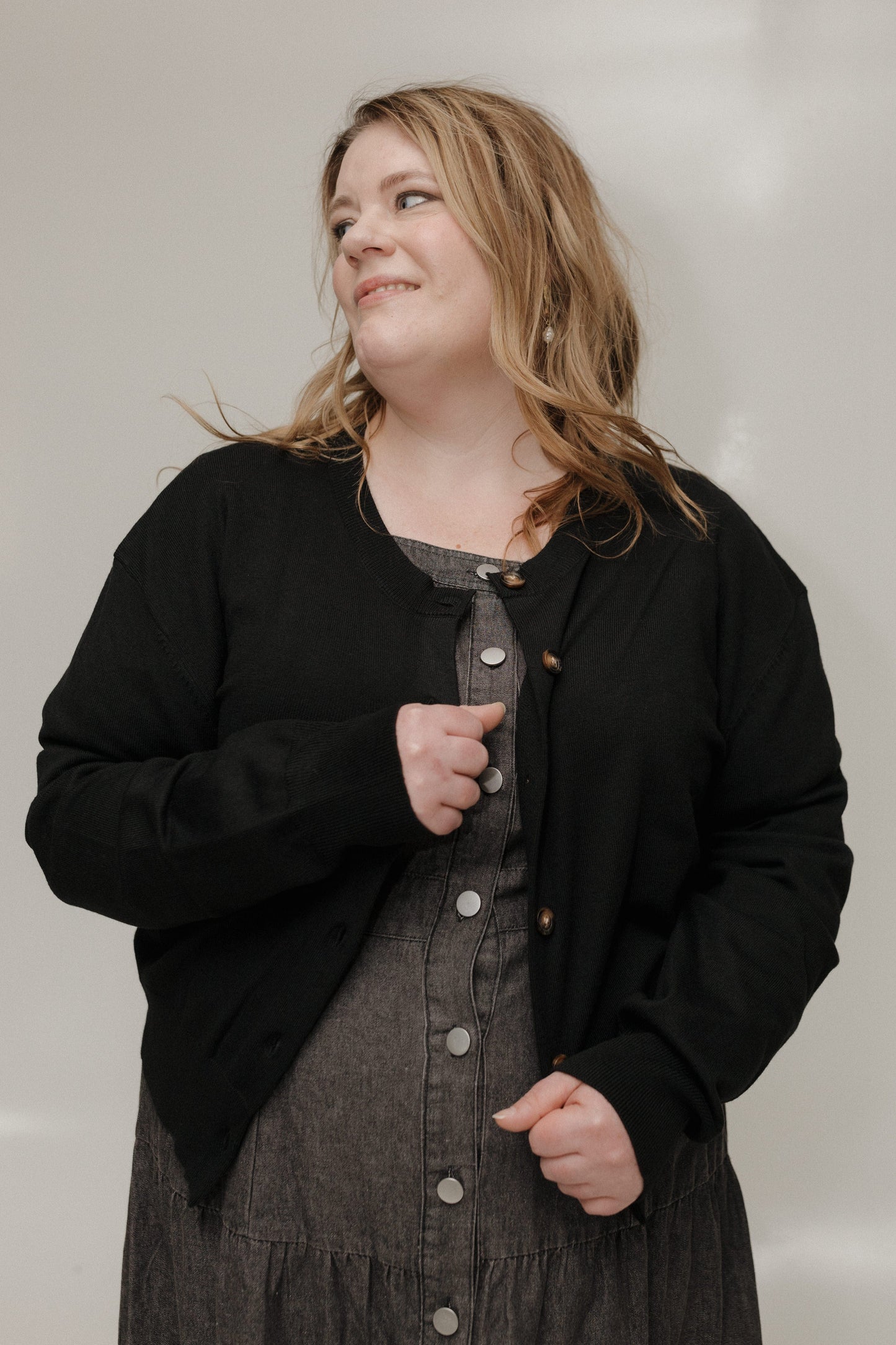 Woman wearing a black cardigan over a gray dress against a plain background