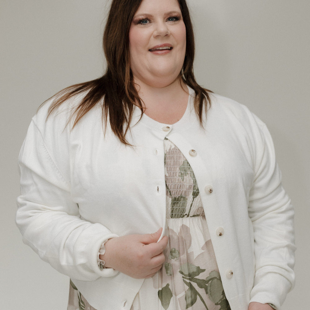 Woman wearing a white cardigan over a floral dress against a plain background
