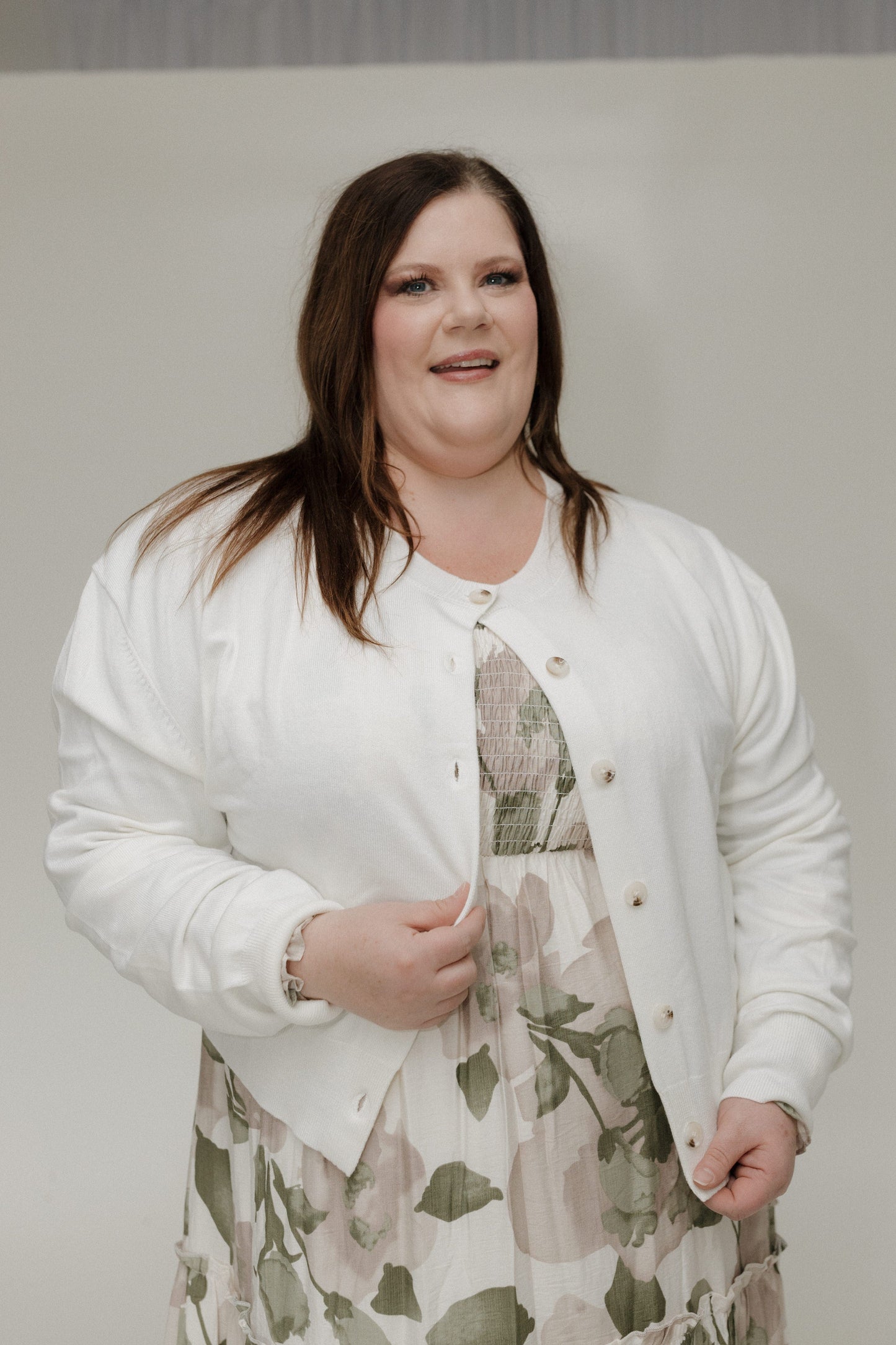 Woman wearing a white cardigan over a floral dress against a plain background