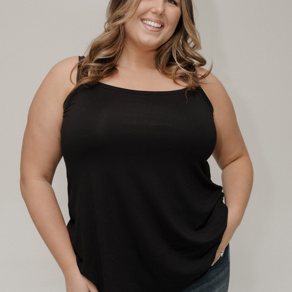 Woman wearing a black sleeveless top and jeans against a plain background