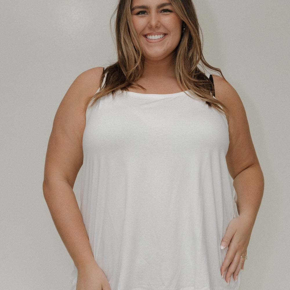 Woman wearing a white sleeveless top against a plain background