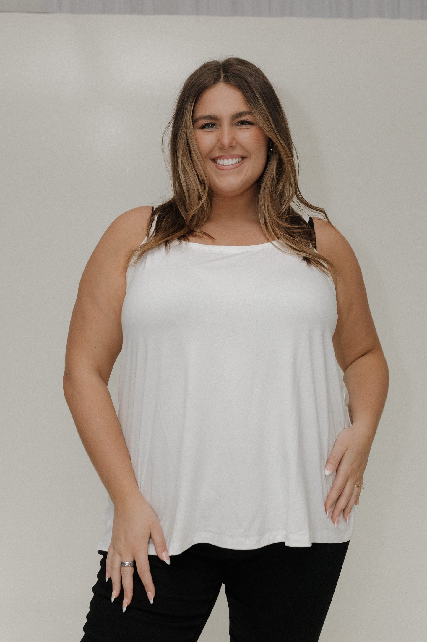 Woman wearing a white sleeveless top against a plain background