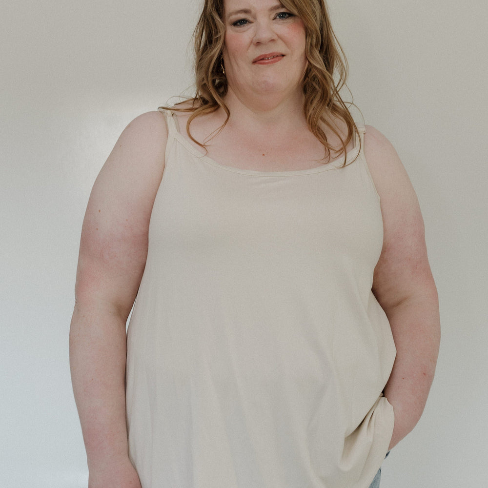 Woman wearing a beige tank top and light blue jeans against a plain background