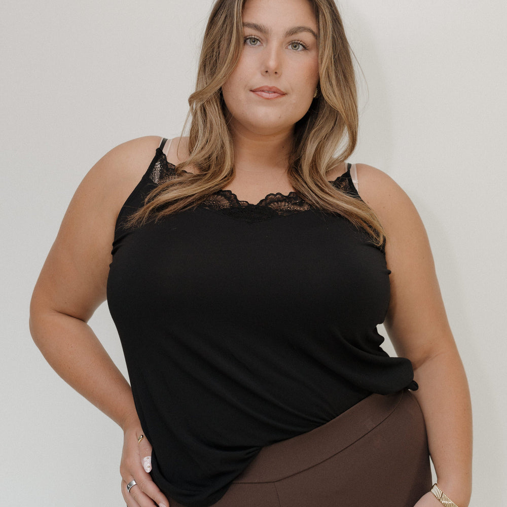 Woman wearing a black top with lace details and brown pants against a white background