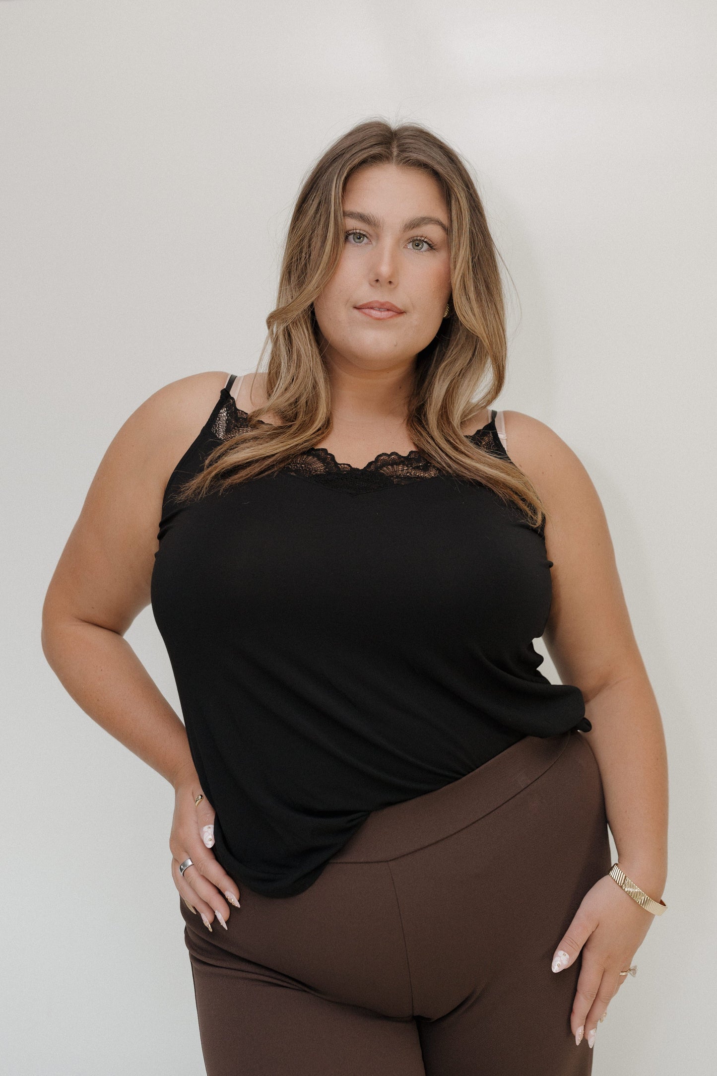 Woman wearing a black top with lace details and brown pants against a white background