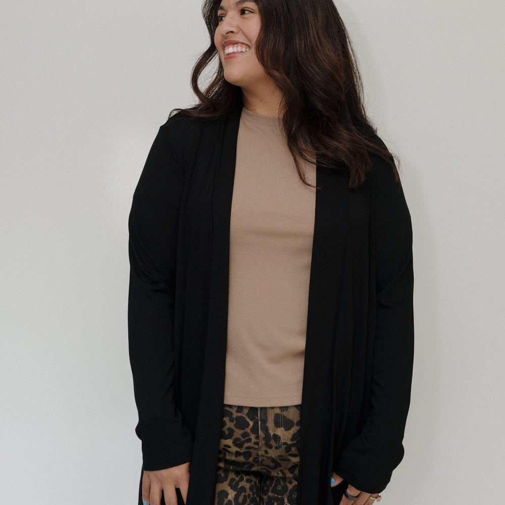 Woman wearing a black cardigan, beige top, and leopard print pants against a white background