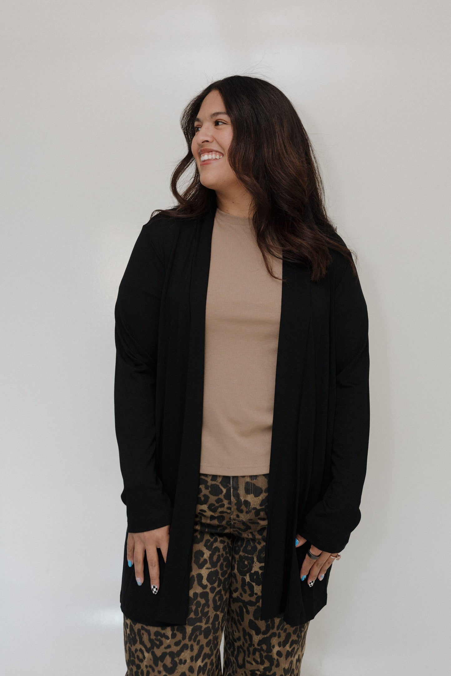 Woman wearing a black cardigan, beige top, and leopard print pants against a white background