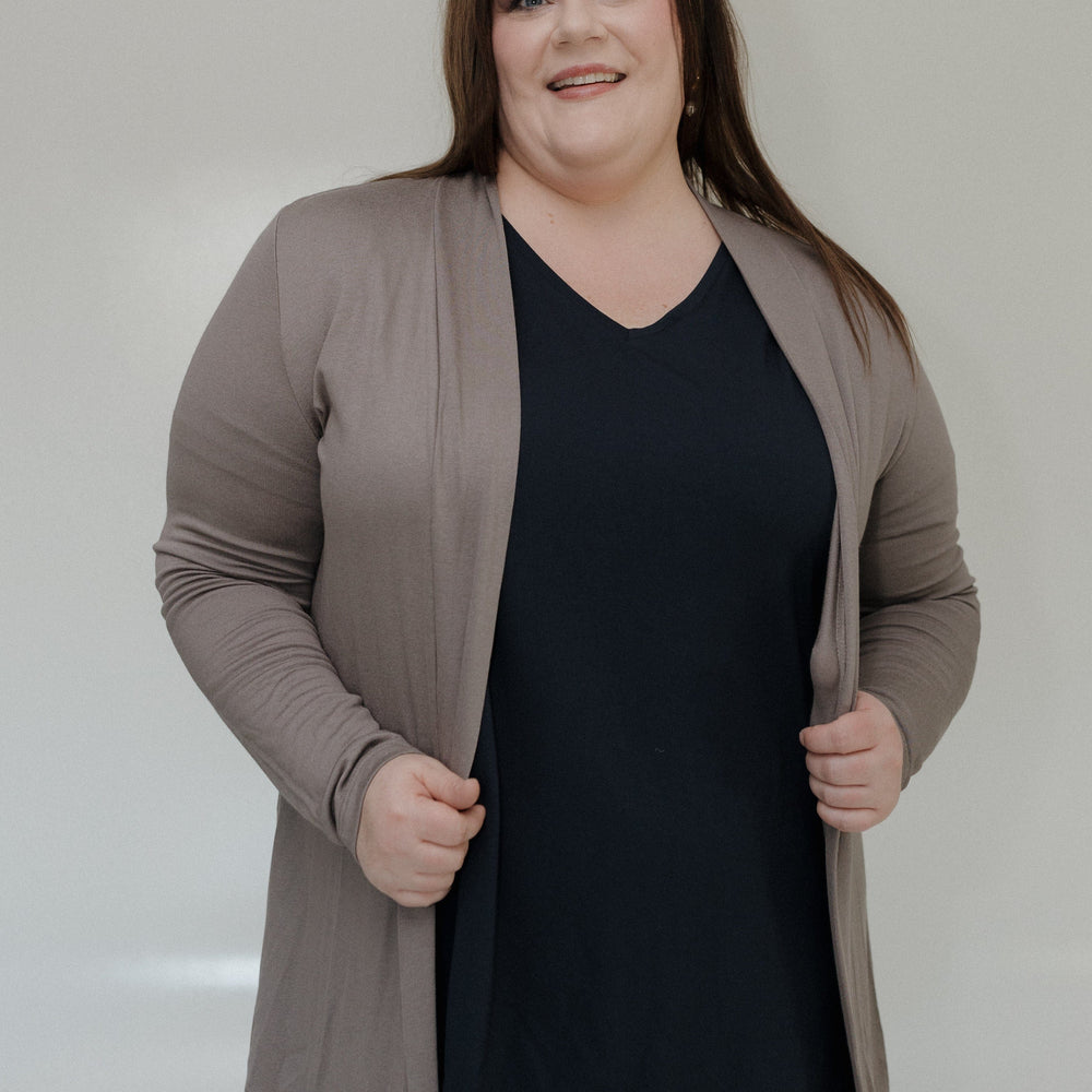 Woman wearing a black top and beige cardigan against a plain background