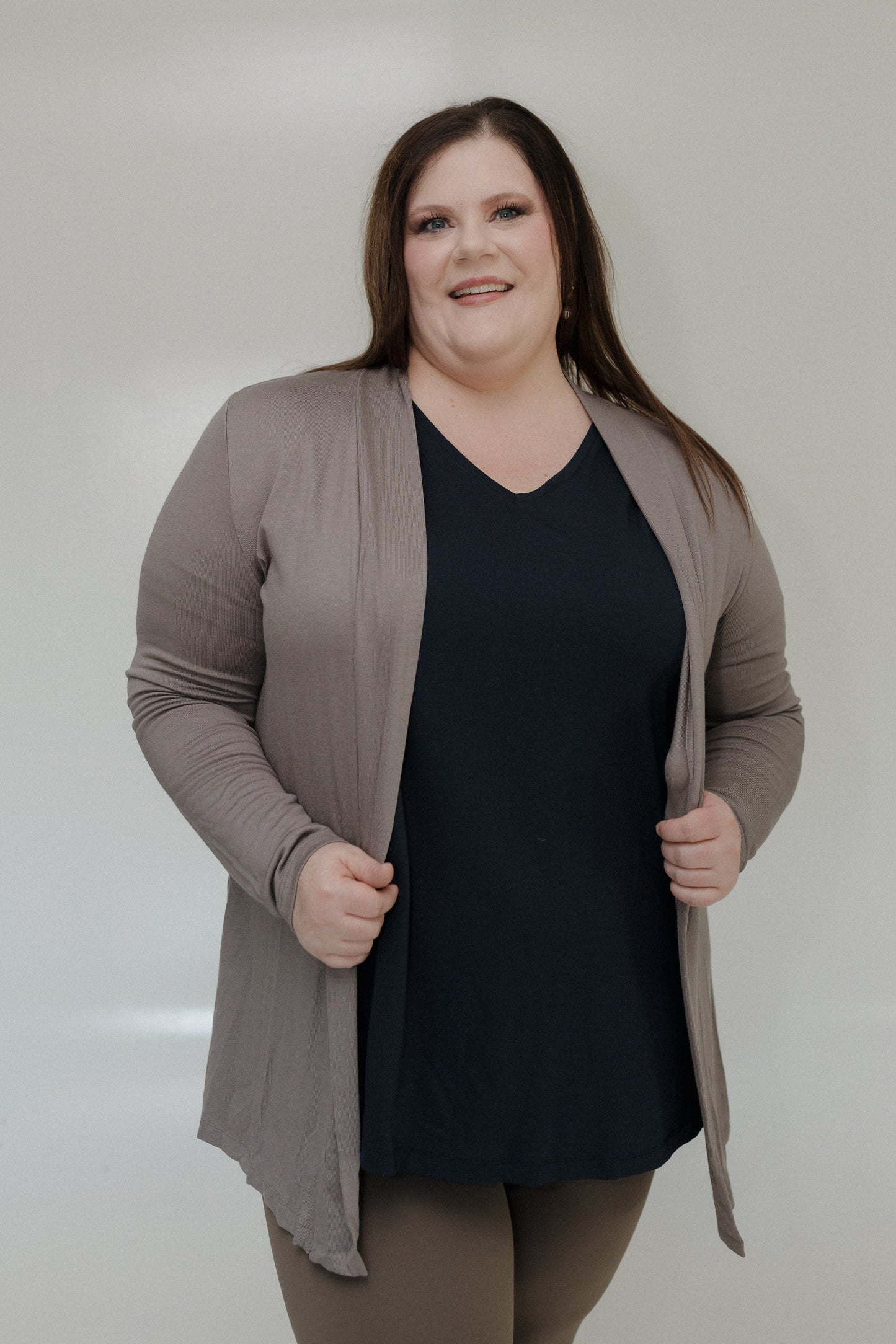 Woman wearing a black top and beige cardigan against a plain background