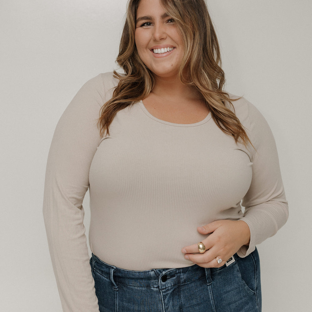 Woman wearing a beige long-sleeve top and blue jeans against a plain background