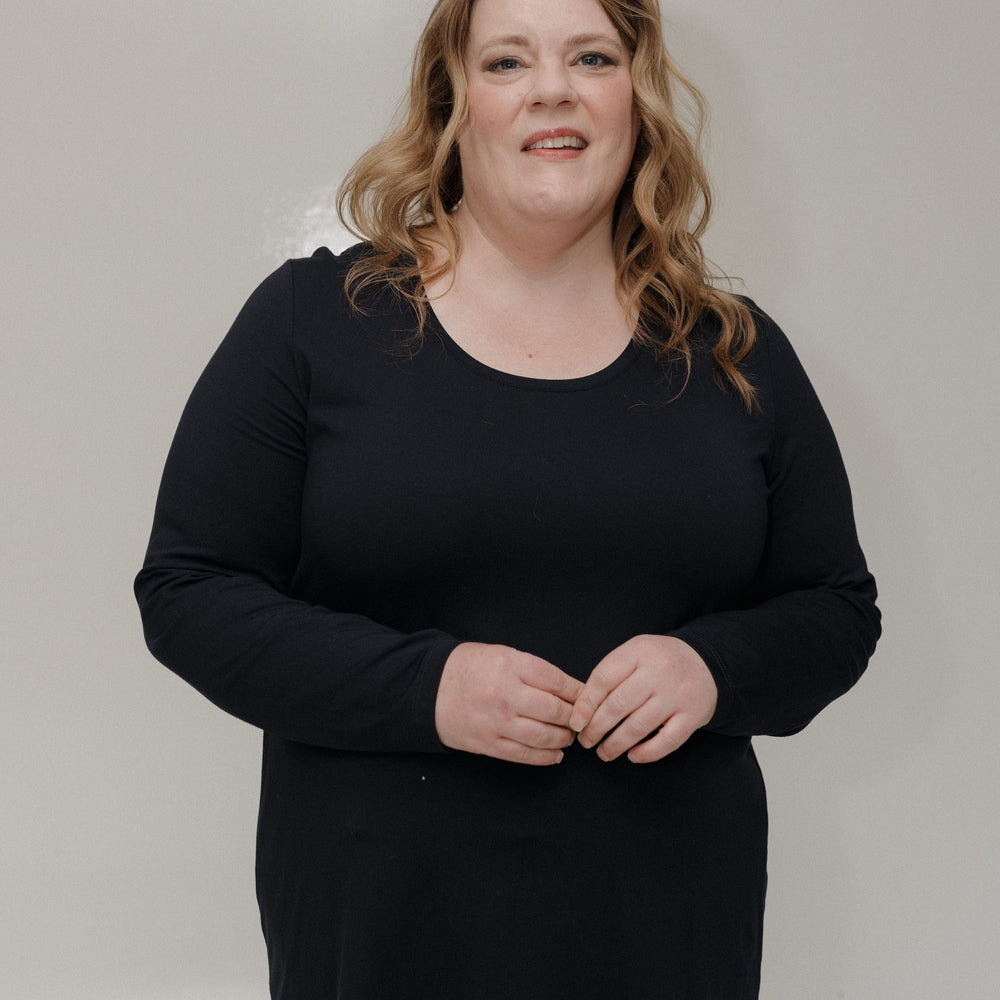 Woman wearing a black top and light blue jeans against a plain background