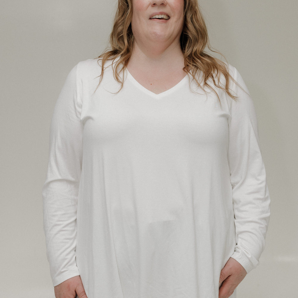 Person wearing a white long-sleeve top and light-colored pants against a plain background