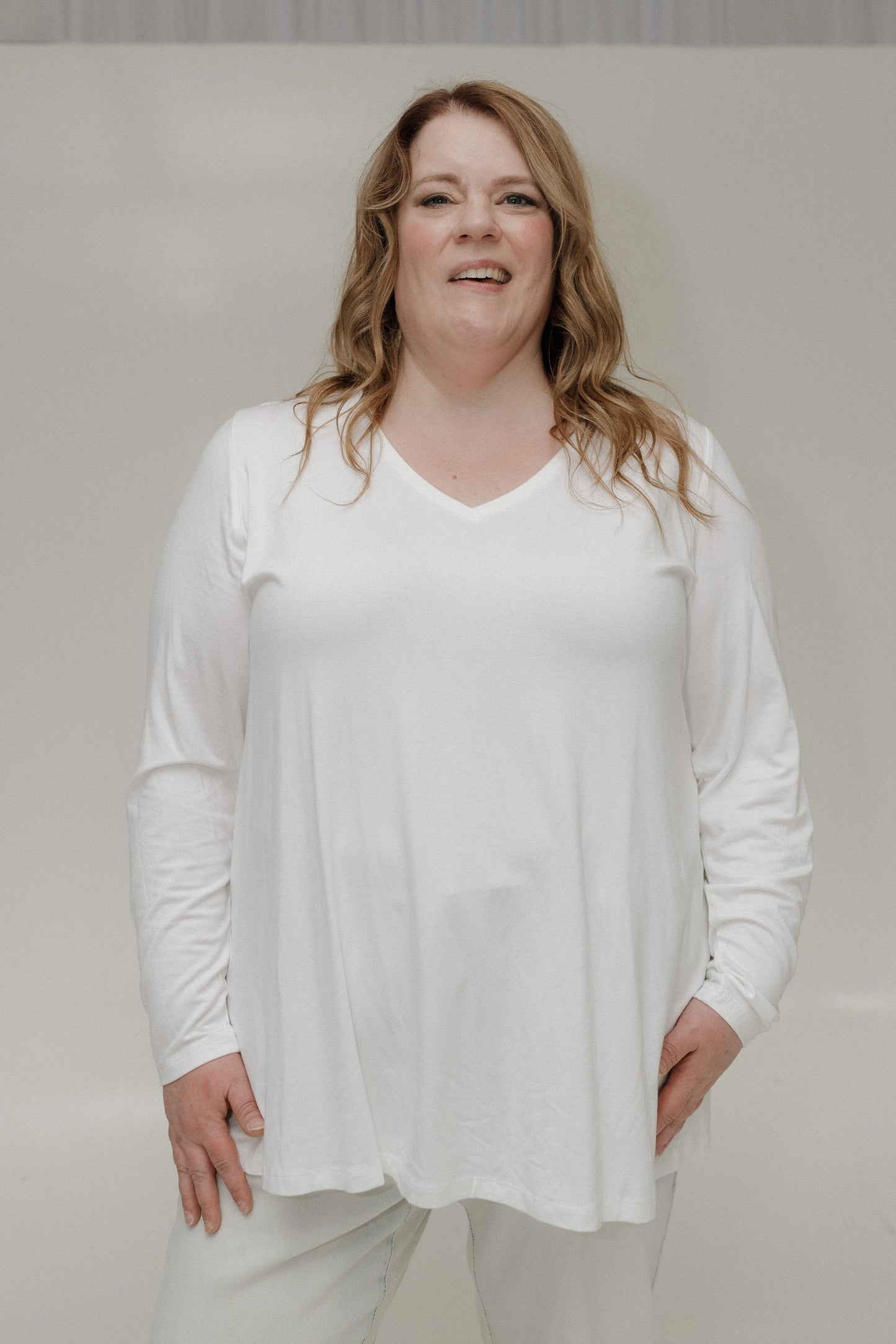 Person wearing a white long-sleeve top and light-colored pants against a plain background