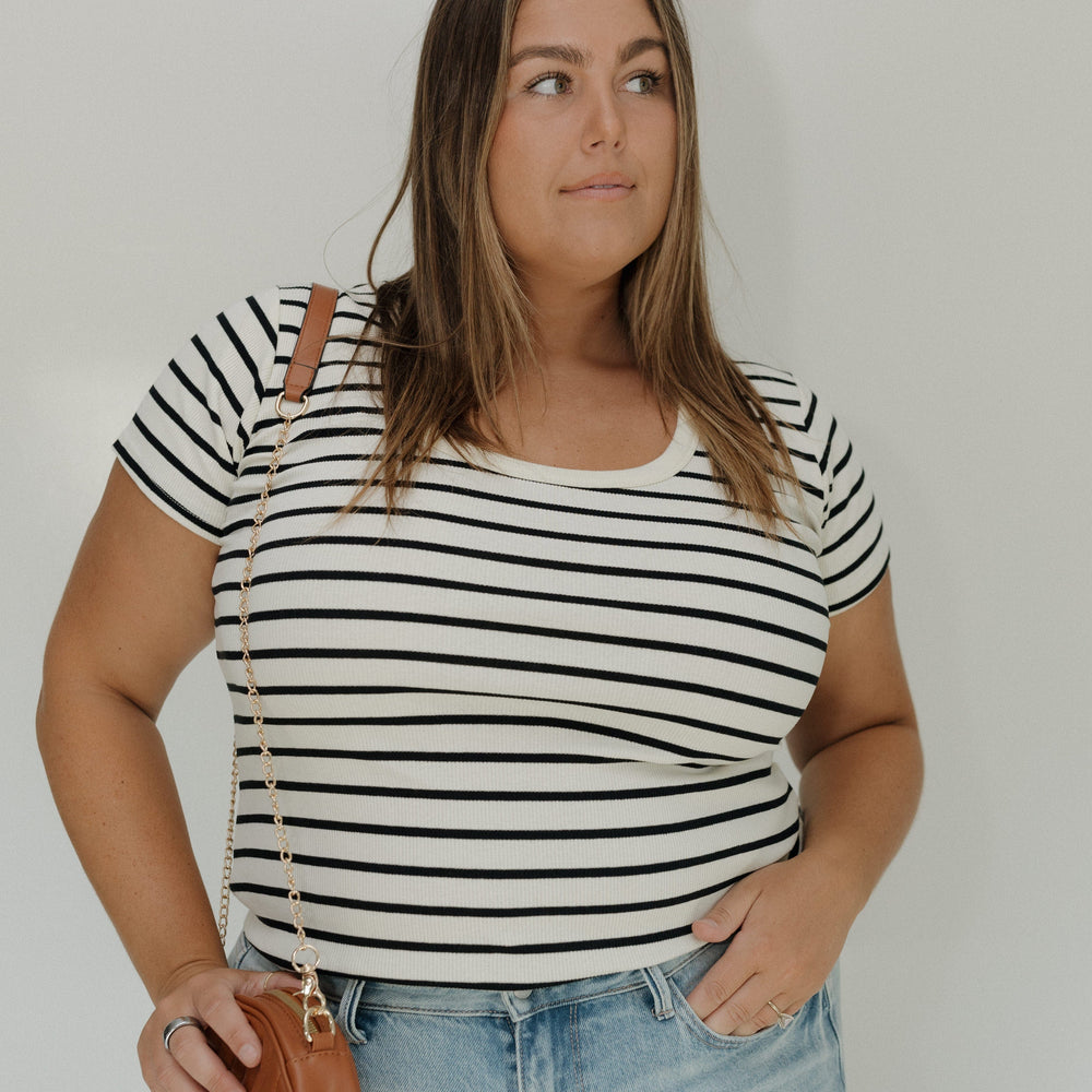 Woman wearing a black and white striped shirt and blue jeans, holding a brown handbag.