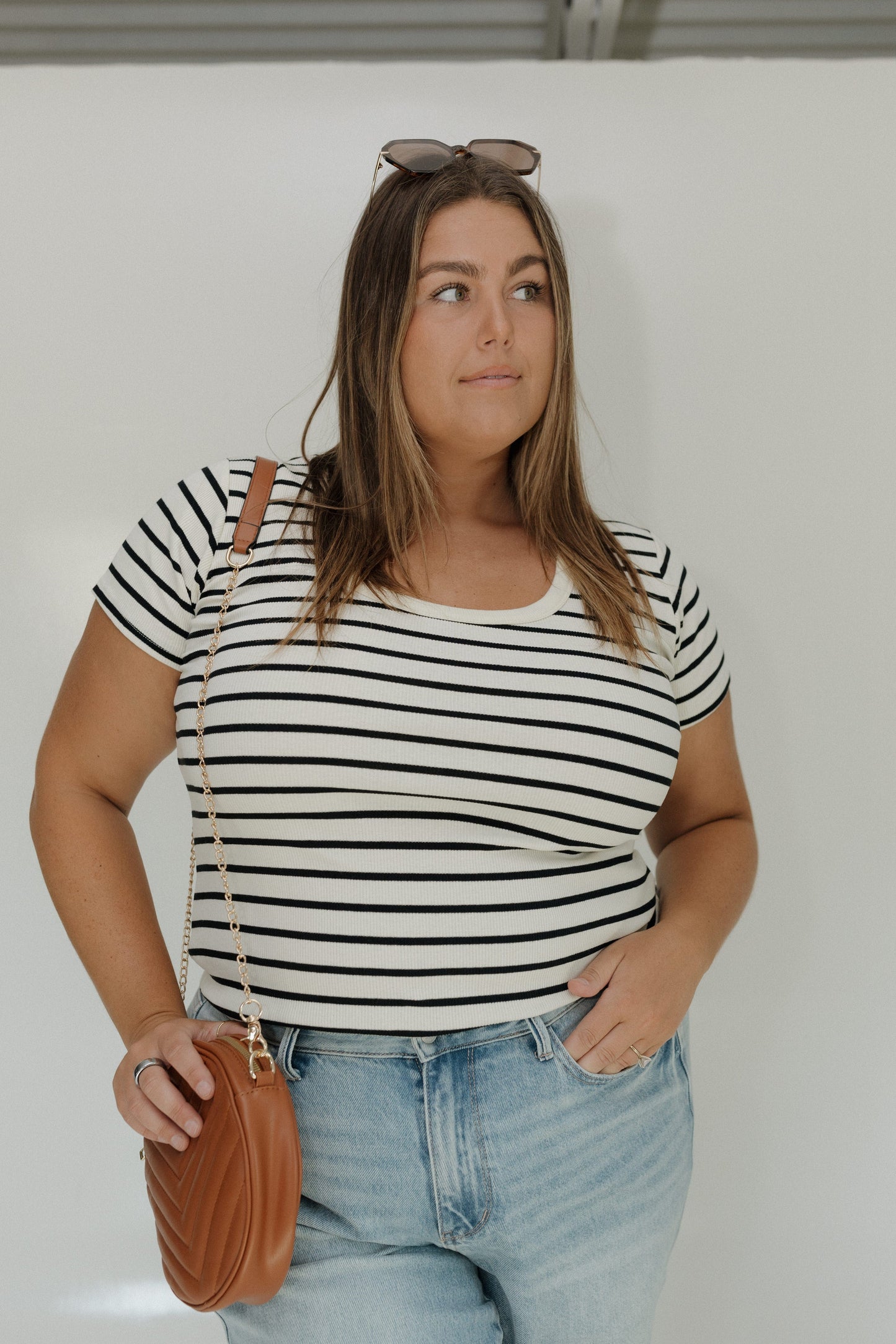 Woman wearing a black and white striped shirt and blue jeans, holding a brown handbag.