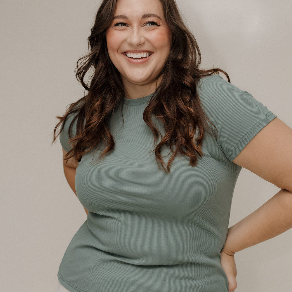 Woman wearing a green t-shirt and white pants against a neutral background