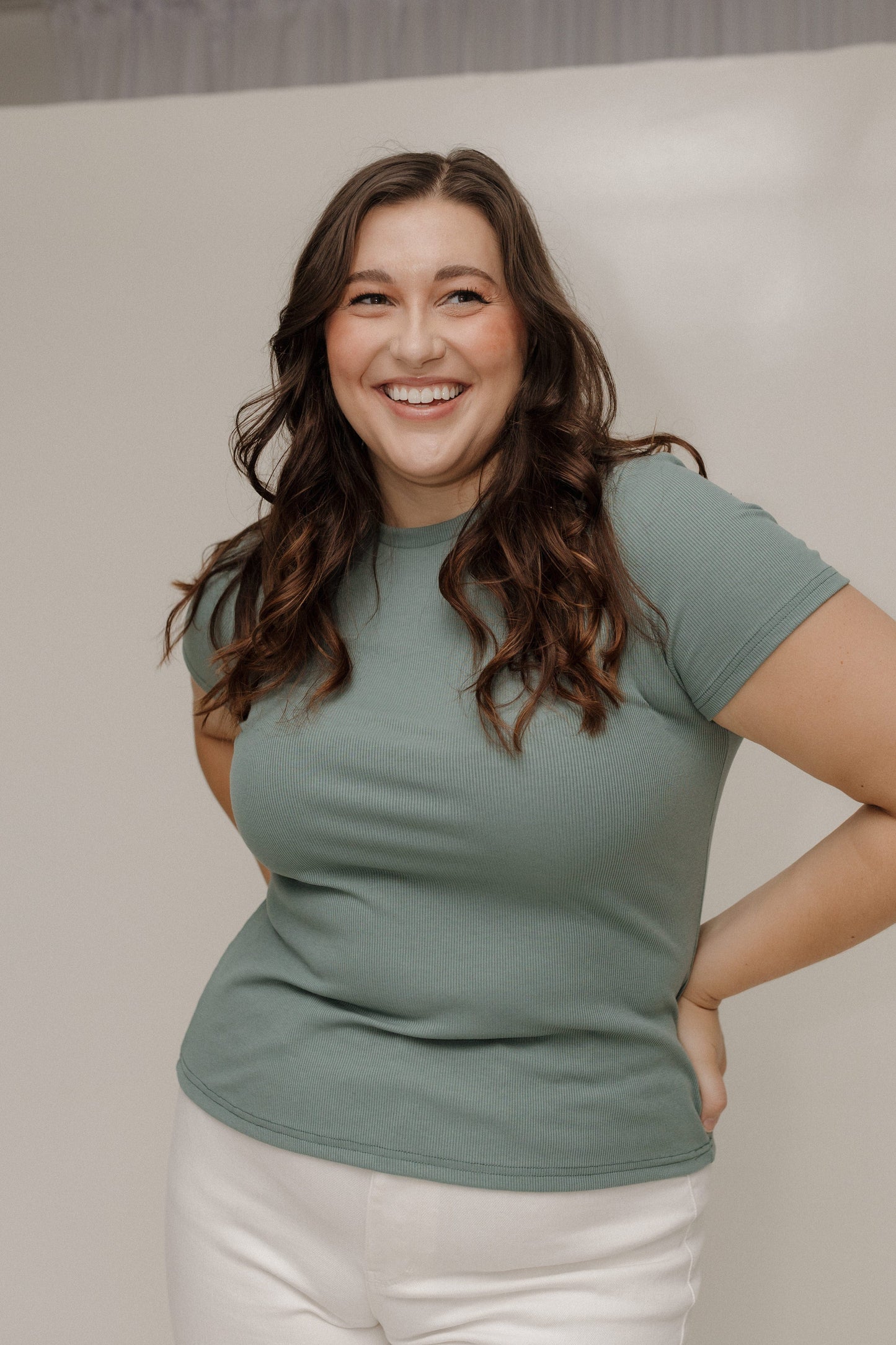 Woman wearing a green t-shirt and white pants against a neutral background